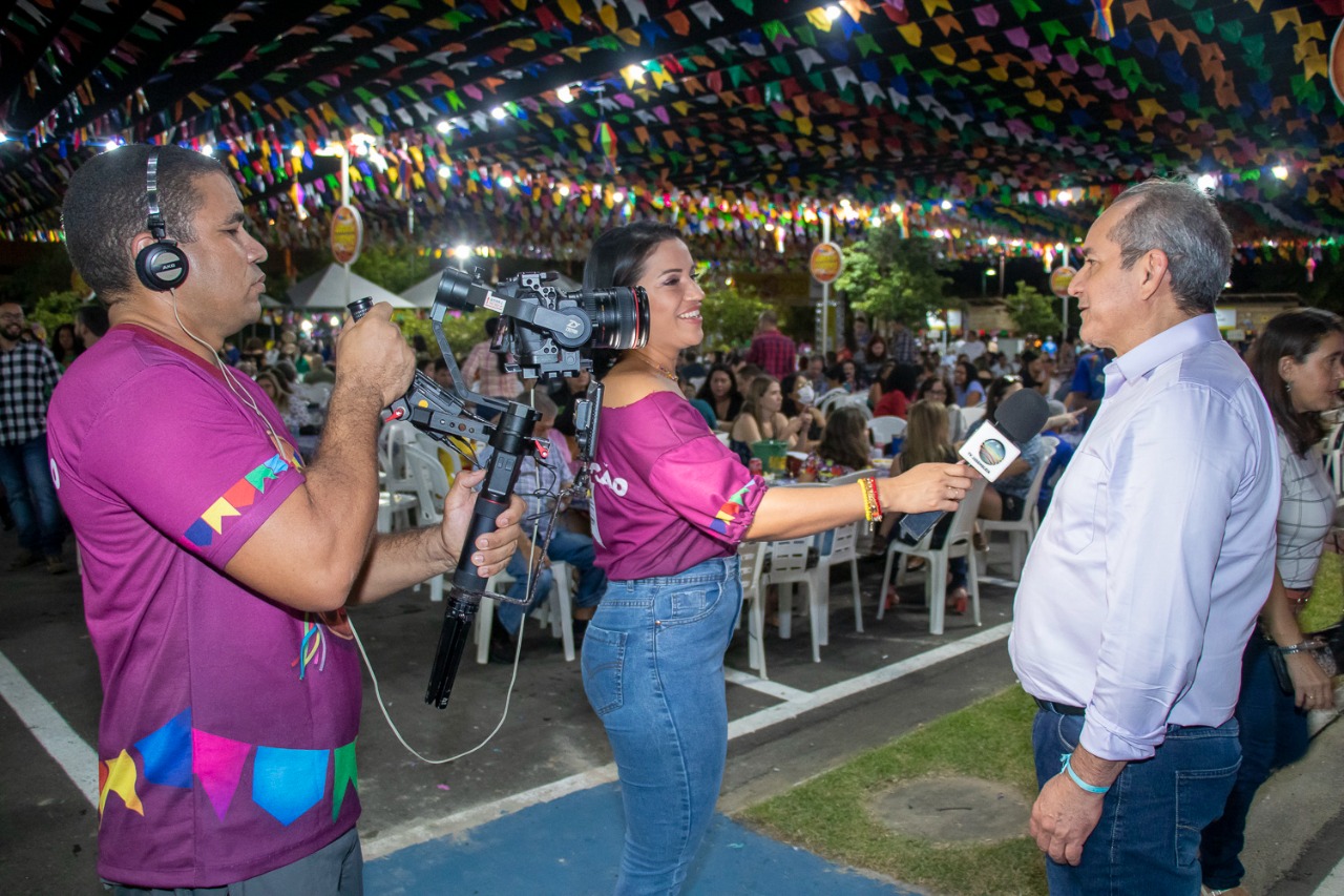 Equipe de reportagem entrevista o público que prestigia o arraial, entre deputados, pessoas da comunidade, brincantes dos grupos folclóricos e autoridades