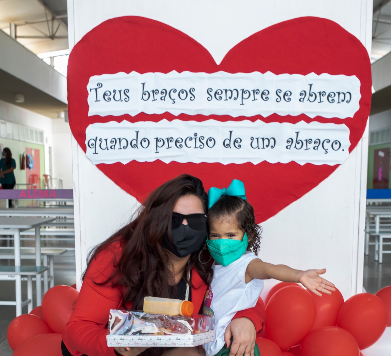 Mãe e filha registram o momento em frente ao cartaz que destaca a importância do abraço materno